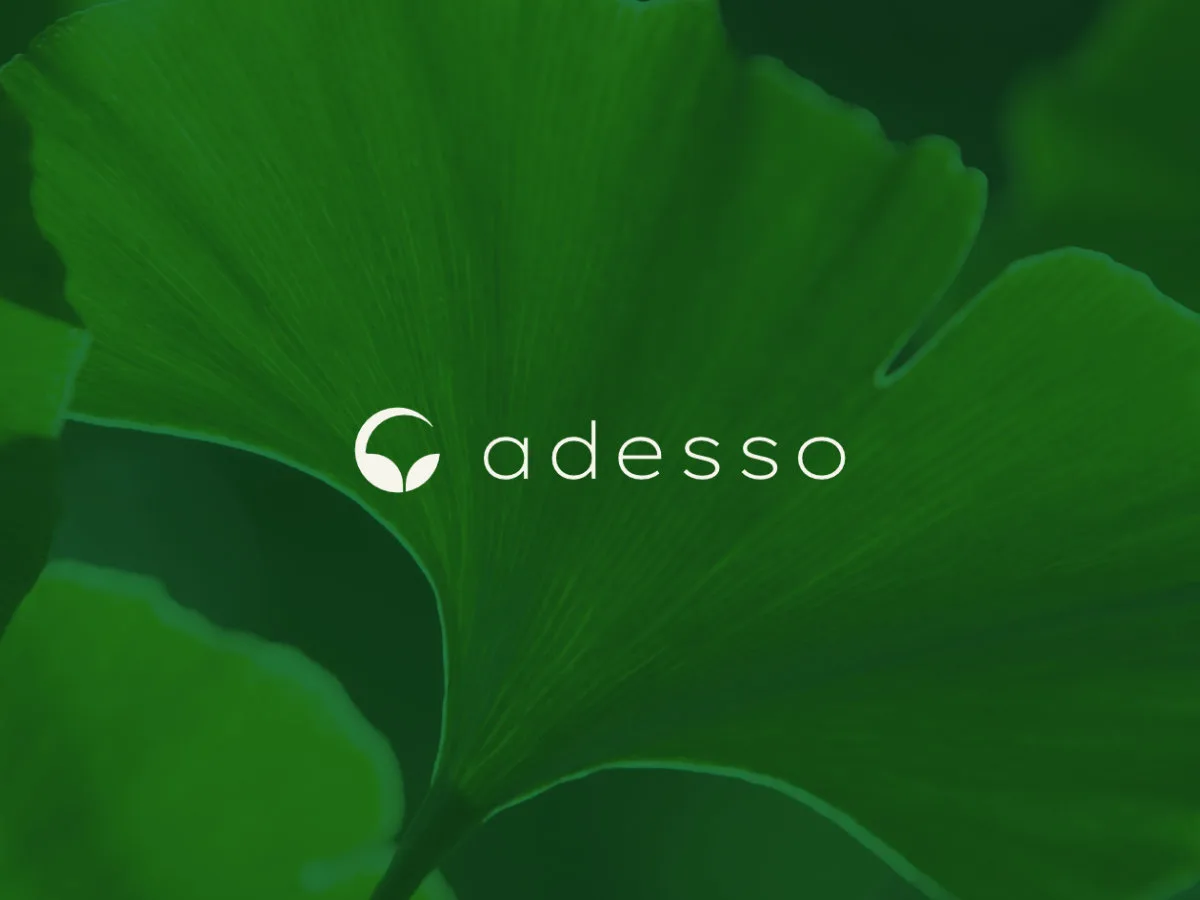 Adesso logo in white, overlaid on a close-up image of a ginkgo leaf.